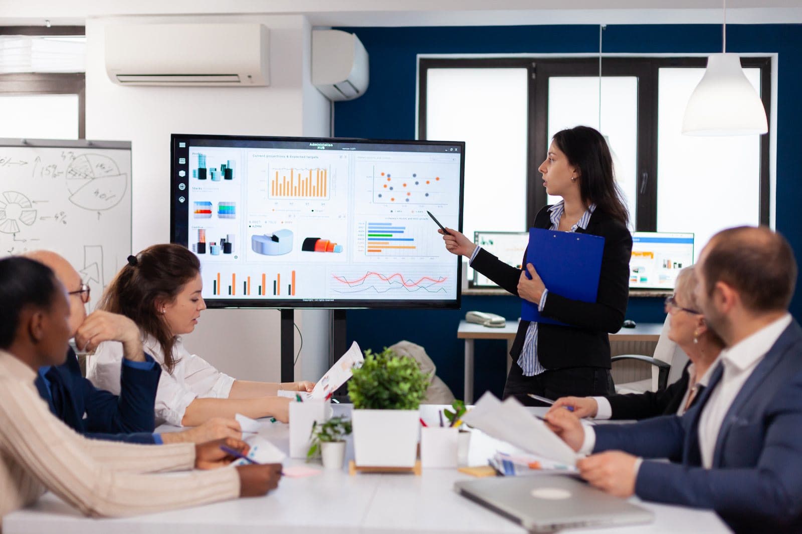A sales leader presenting projections and targets on a large screen to her team in a meeting room